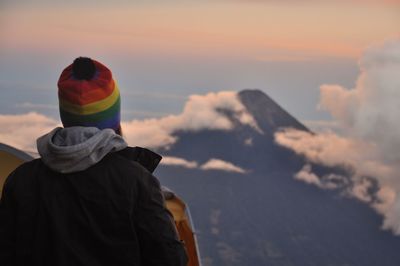 Rear view of man looking at mountain against sky during sunset