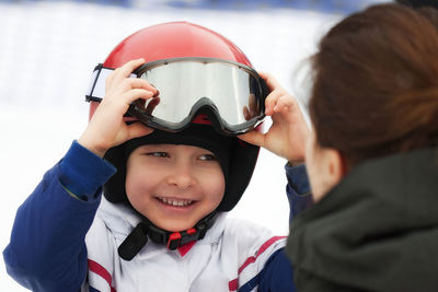 Cheerful boy in red helmet and ski goggles smiling to his mother. winter sports, young skier