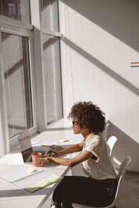 Side view of woman using mobile phone while sitting in office