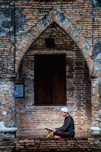 Man sitting on brick wall of building