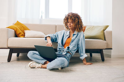 Young woman using laptop while sitting on sofa at home