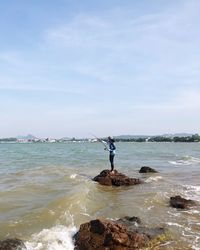 Woman standing on rock in sea against sky