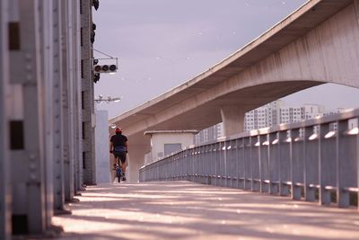Rear view of man riding bicycle on bridge