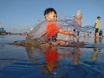 Cute boy playing in water against sky