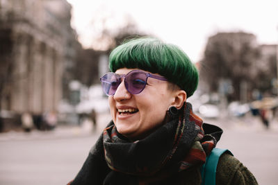 Portrait of happy punk woman in purple sunglasses standing in city