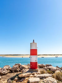 Lighthouse by sea against clear blue sky