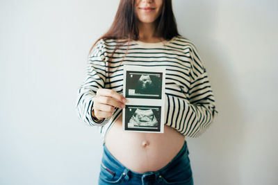 A woman in anticipation of the birth of a child holds an ultrasound scan in front of her.