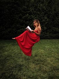 Side view of teenage girl reading book while levitating over grassy field