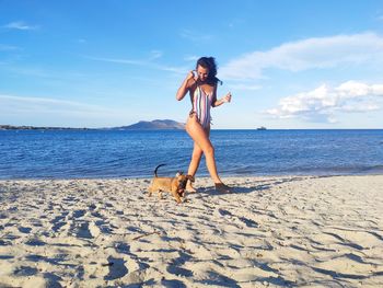 Full length of woman and her puppy dog at beach against sky