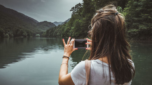 Rear view of woman photographing lake