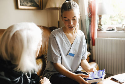 Female healthcare with medicine box talking with senior woman in living room