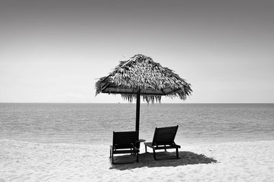 Chairs below thatched roof parasol on shore at beach