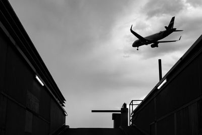 Low angle view of silhouette airplane flying in building against sky and a boom barrier. 