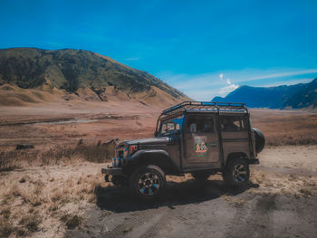 Vintage car on field against mountain range and blue sky