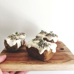 Cropped image of person holding tin cakes in wooden board against wall