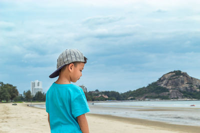Boy standing on beach by sea against sky