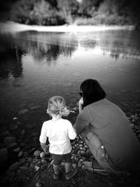 Rear view of woman crouching by daughter at lakeshore