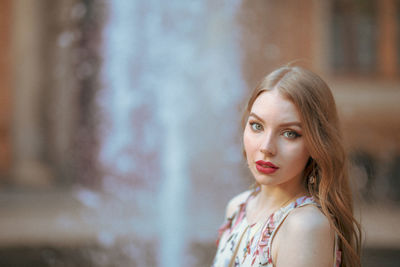 Portrait of beautiful young woman standing against fountain in city