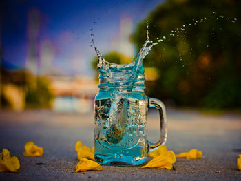 Close-up of water splashing in jar amidst flowers on road