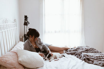 Young woman playing with dog while relaxing on bed at home