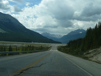 Empty road by mountains against cloudy sky