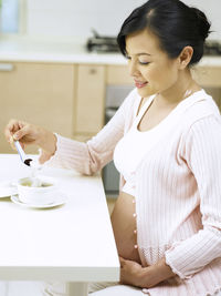 Pregnant woman having food at table in home