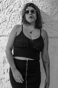 Portrait of young woman wearing sunglasses standing against wall