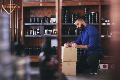 Salesman kneeling while writing on paper by rack in deli