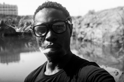 Portrait of mature man wearing eyeglasses while smoking against lake