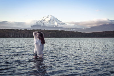 Woman standing by lake against mountain range