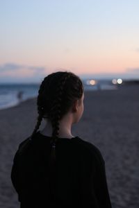 Rear view of teenage girl with braided hair standing on beach against clear sky