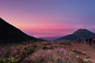 People walking on mountain against sky during sunset