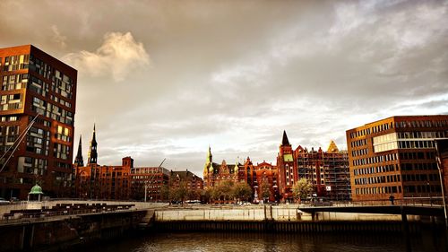 Buildings by river against cloudy sky