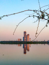 Scenic view of lake by buildings against sky during sunset