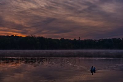 Man rowing boat on lake against sky during sunset