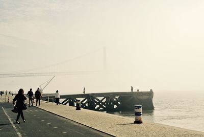 People walking on bridge over sea against sky