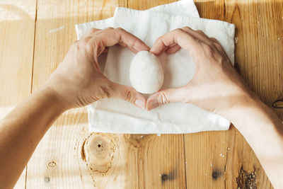 Female hands making heart shape holding a handmade ceramic egg for easter. 