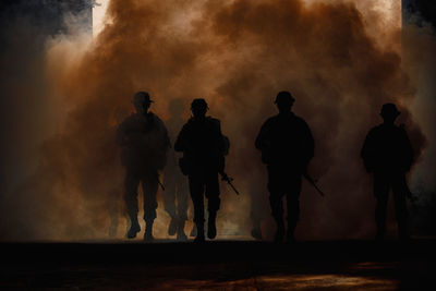 Silhouette army soldiers amidst smoke at sunset
