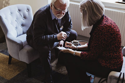 High angle view of senior woman showing mobile phone to man while sitting in hotel