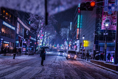 People and cars on city street during winter at night