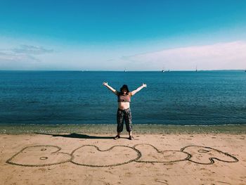 Woman with arms outstretched standing by text at beach