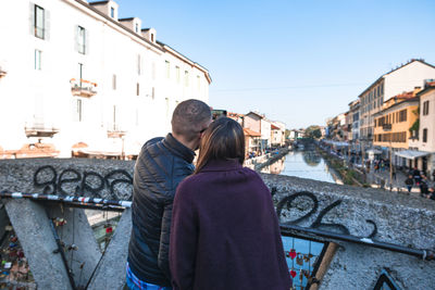 Rear view of couple standing on canal in city