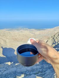 Cropped hand of woman holding coffee at beach