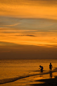 Silhouette people on beach against sky during sunset