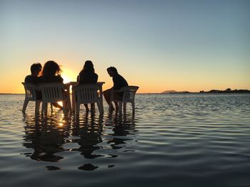 People sitting by swimming pool against sky during sunset