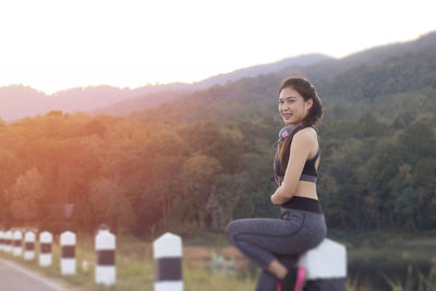 Side view of smiling young woman standing on road against mountains