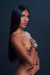 Portrait of naked woman covering breast while standing against gray background