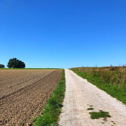 Road amidst field against clear blue sky