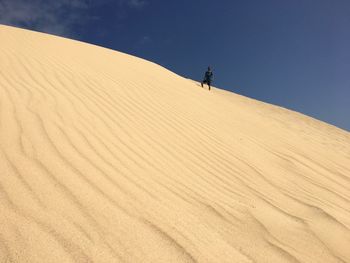 Man on sand dune in desert against sky