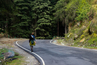 Rear view of man walking on road along trees